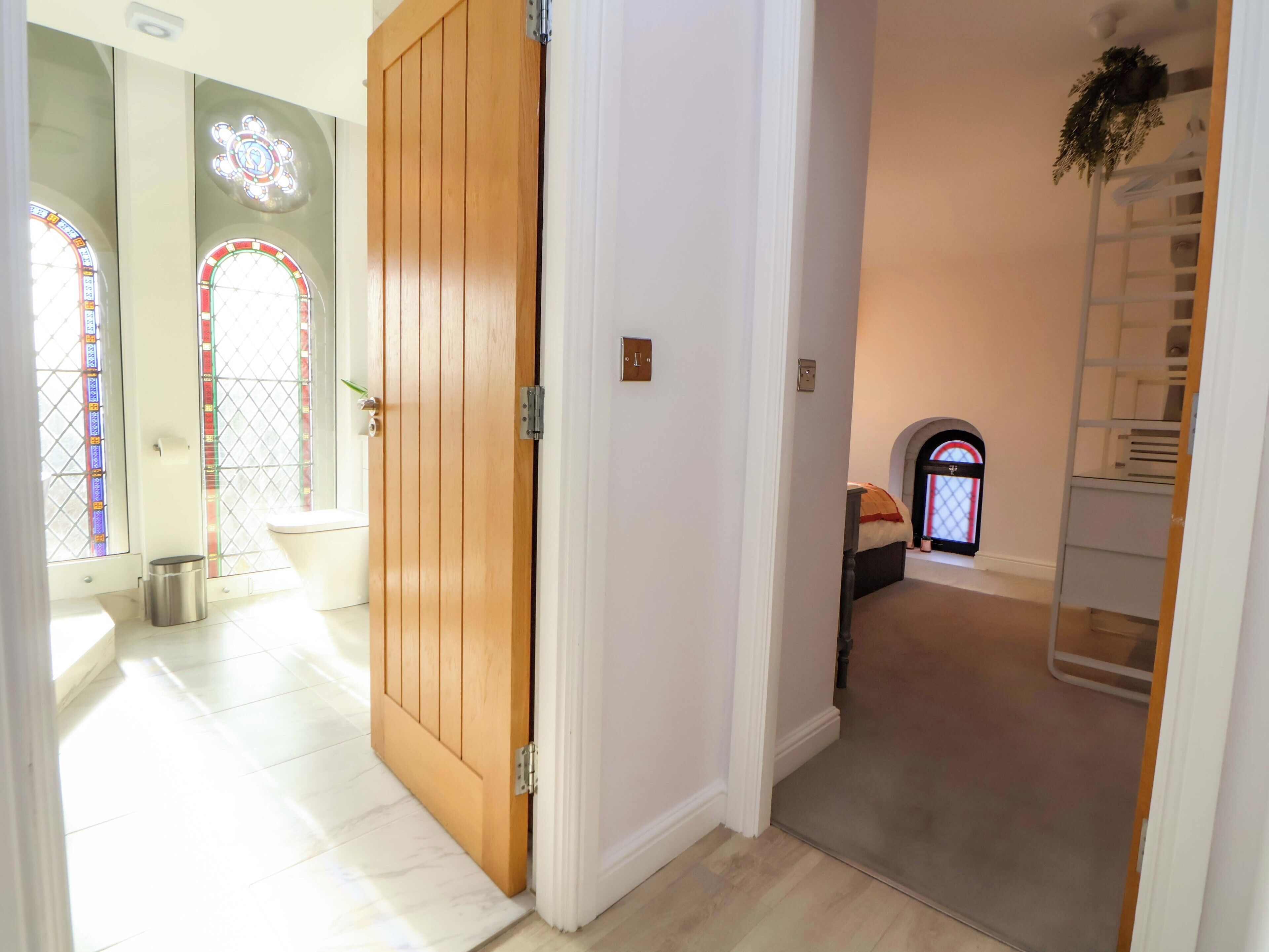 A hallway with a wooden door, a white wall, and a staircase with a railing.