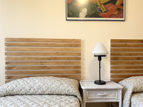 Una habitació amb dos llits, una tauleta de nit amb una làmpada i un quadre a la paret.