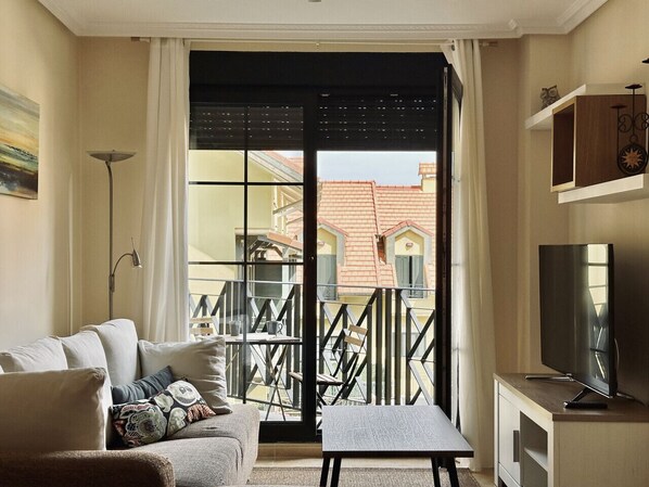 Een woonkamer met een bank, salontafel, televisie en een balkon met hekwerk.