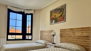 A room with two beds, a window with curtains, a painting on the wall, and a lamp on a bedside table. - Apartment Rinco Ris - 6045 (Noja)