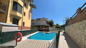 A swimming pool with a tiled deck, surrounded by a stone wall and a metal fence. - Apartment Rinco Ris - 6045 (Noja)