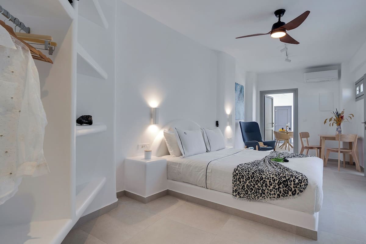 A modern bedroom with a bed, nightstands, a ceiling fan, and a dining area with chairs and a table.
