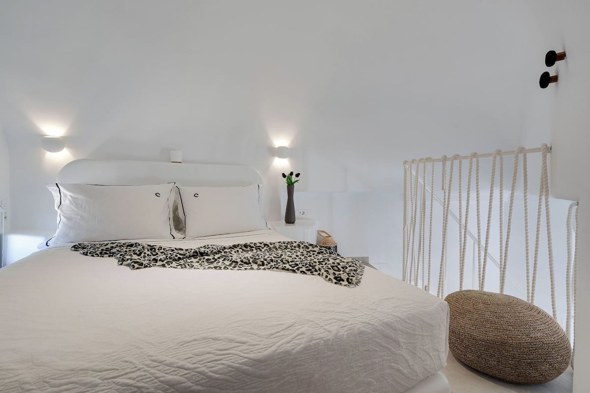 A bedroom with a bed, a bedside table with a vase, and a rope curtain.