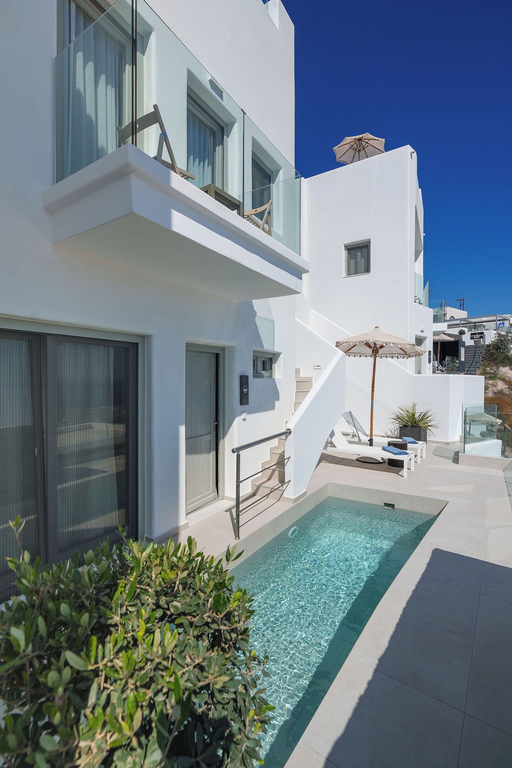 A modern white building with a pool, a staircase, and a lounge area with a sun umbrella.