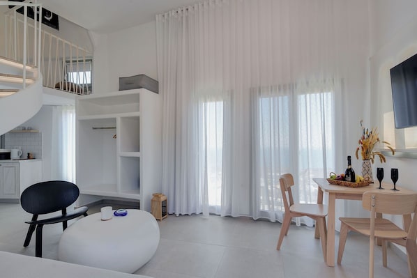 A modern living room with a dining area, a staircase, and large windows with sheer curtains. - SantoView Villas (Vourvoulos)