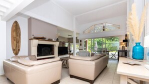 A spacious living area with a fireplace, two sofas, a TV, and a dining area with a view of the outdoors. - Villa Cormoran (MOLIETS ET MAA)