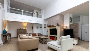 A spacious living area with a high ceiling, a fireplace, a television, and a dining table. - Villa Cormoran (MOLIETS ET MAA)
