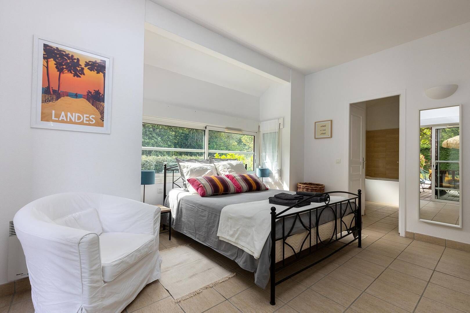 Ein Schlafzimmer mit Bett, Sessel, Nachttisch und Fenster mit Blick auf Grünflächen.