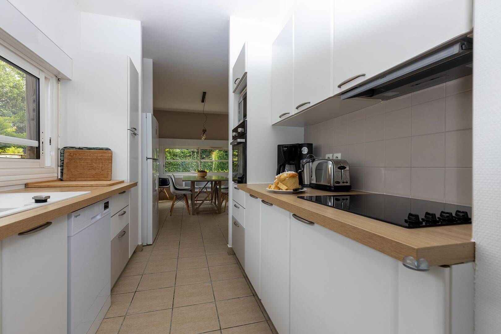 A modern kitchen with white cabinets, a wooden countertop, and a dining area with a table and chairs.