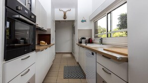 A narrow kitchen with white cabinets, a black oven, and a wooden countertop. - Villa Cormoran (MOLIETS ET MAA)