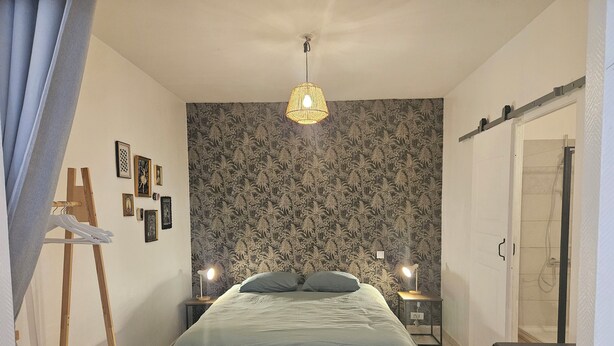 A bedroom with a bed, two bedside lamps, a wooden easel, and a wardrobe. - Apartment 40 m² near the Canal de la Robine (Narbonne)