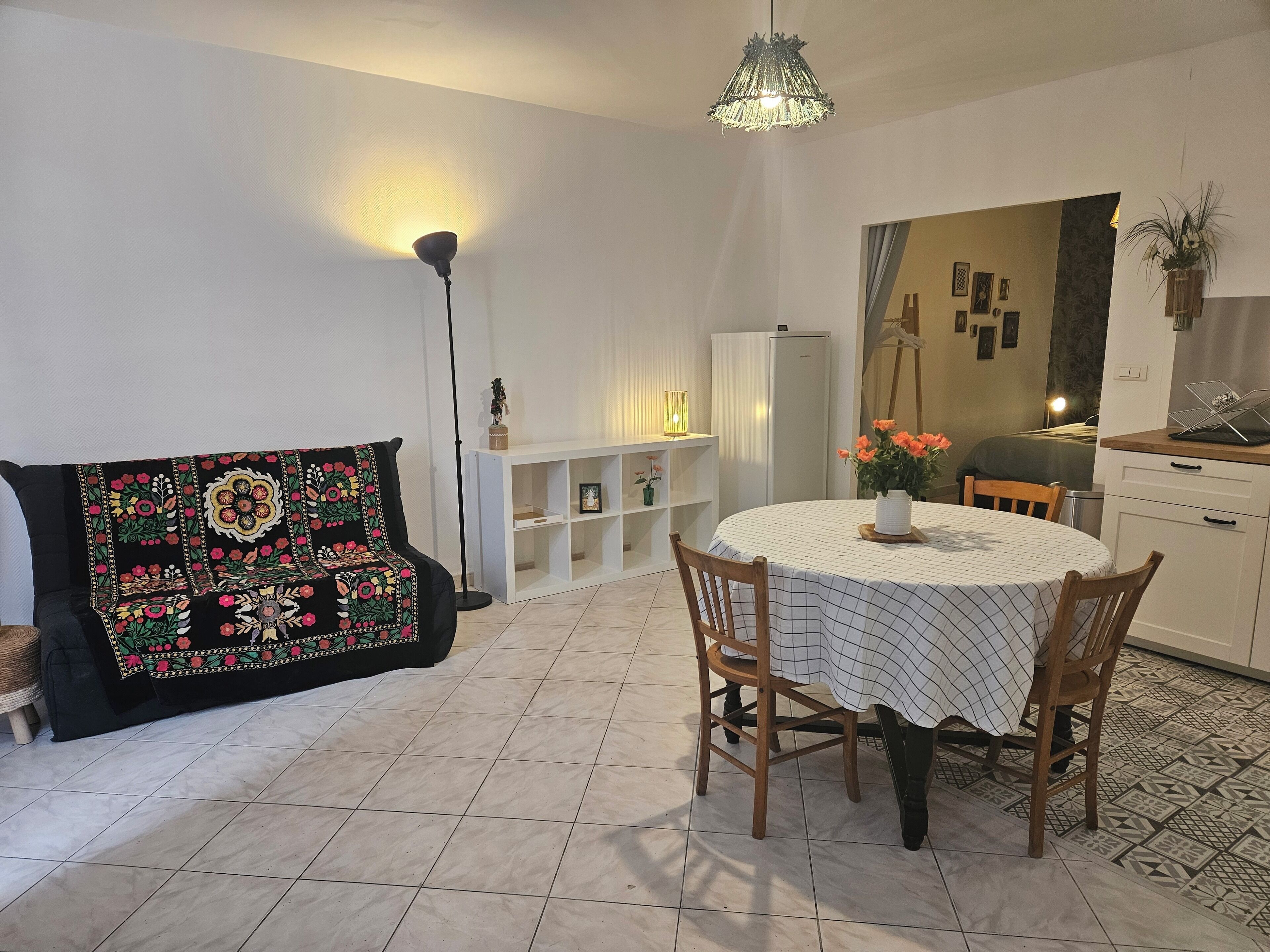 A cozy living room with a sofa, a dining table with chairs, a white cabinet, and a patterned throw.
