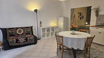 A cozy living room with a sofa, a dining table with chairs, a white cabinet, and a patterned throw.