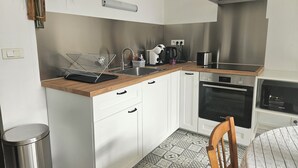 A modern kitchen with white cabinets, a stainless steel range hood, a built-in oven, and a coffee maker. - Apartment 40 m² near the Canal de la Robine (Narbonne)