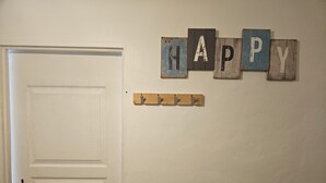 A white door with a simple handle, a wall-mounted wooden sign with the word "HAPPY," and a small wooden shelf with three hooks. - Apartment 40 m² near the Canal de la Robine (Narbonne)