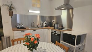 A modern kitchen with white cabinets, a stainless steel range hood, a microwave, and a sink. - Apartment 40 m² near the Canal de la Robine (Narbonne)