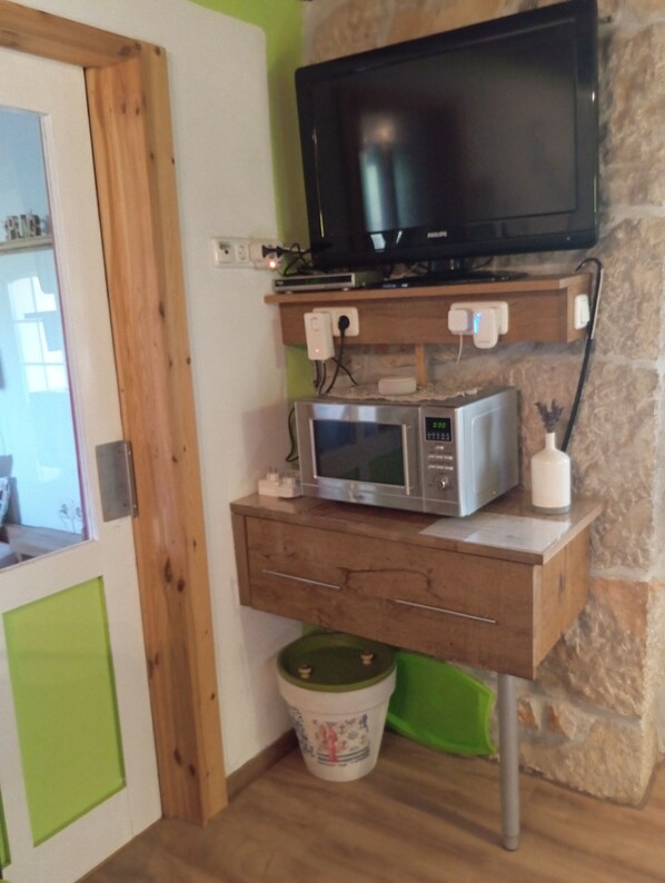 Een kamer met een houten kastje waarin een televisie, een magnetron en een klein witte bakje staan.