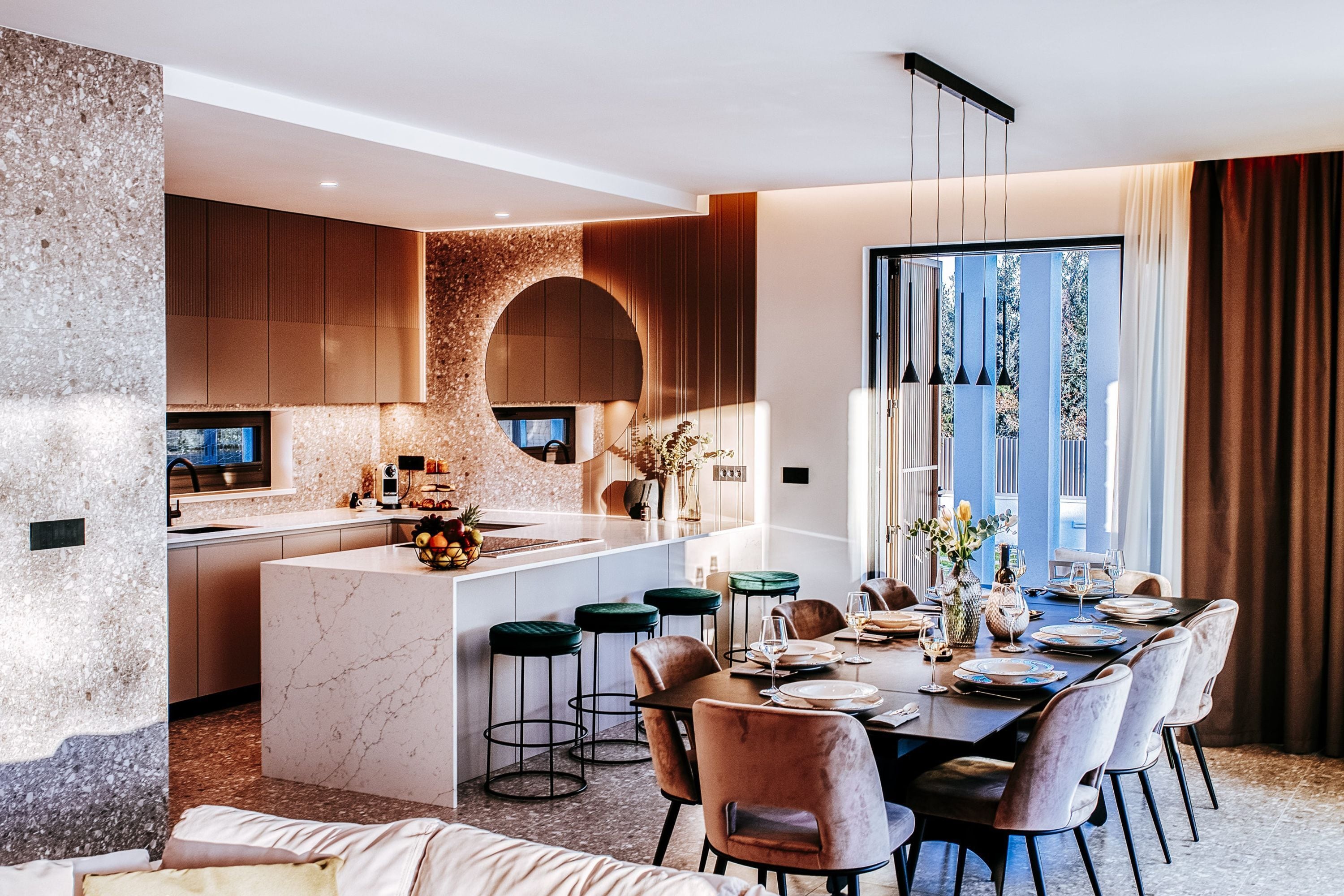 Una cocina moderna con una isla central, taburetes de bar y un comedor con mesa dispuesta para seis personas.