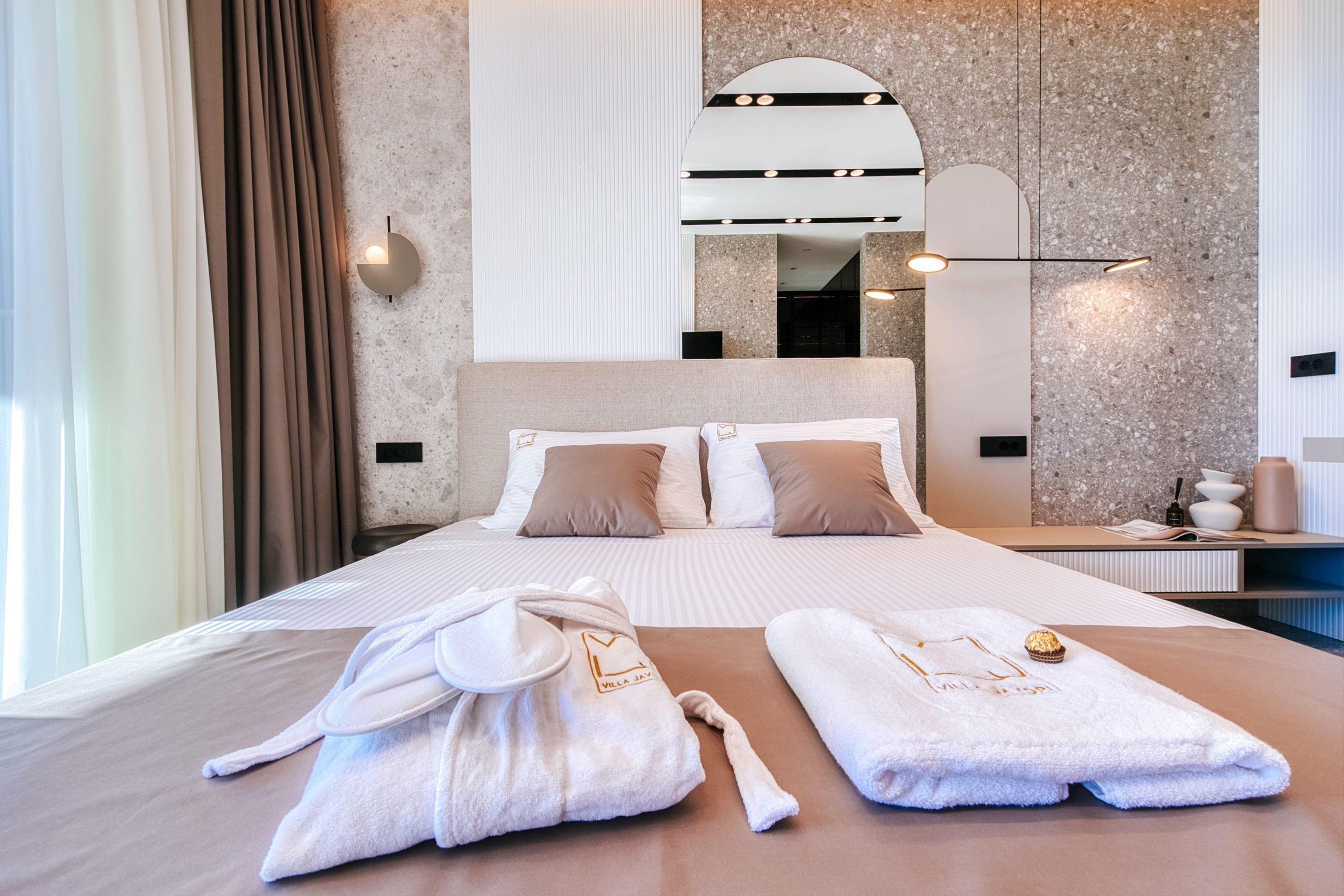 Habitación de hotel con una cama grande, dos toallas, una bata y una mesita de noche con lámpara.