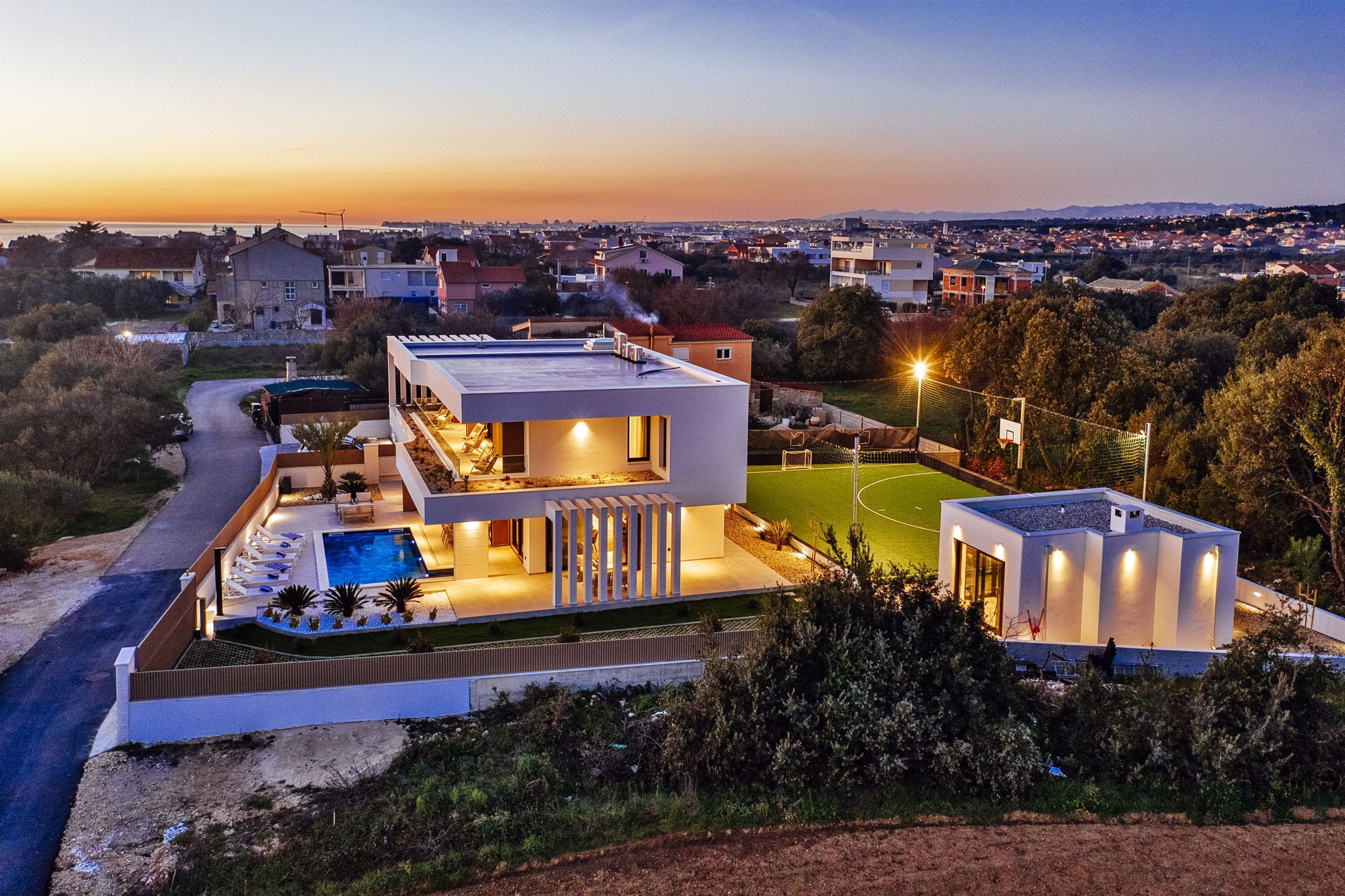 Una casa moderna con piscina, cancha de tenis y vistas del barrio circundante.