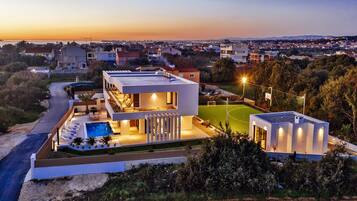 Una casa moderna con piscina, cancha de tenis y vistas del barrio circundante.