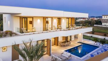 Una casa moderna de dos pisos con piscina, mobiliario exterior y una terraza bien iluminada.