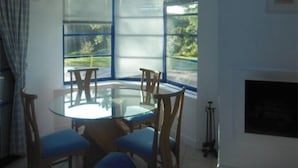 Un comedor con una mesa redonda de vidrio y sillas de madera, un ventanal con persianas y una chimenea.