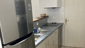 Una cocina con un refrigerador de acero inoxidable, armarios blancos, una encimera y suelo de baldosas.