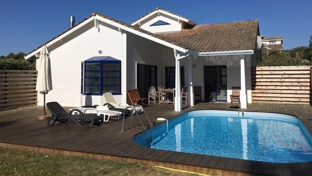 Una casa con piscina, un patio con sillones de descanso y un espacio exterior cubierto.