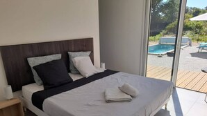 Ein modernes Schlafzimmer mit einem großen Bett, einem Holzkopfende und Blick auf einen Pool und Sitzgelegenheiten im Freien.