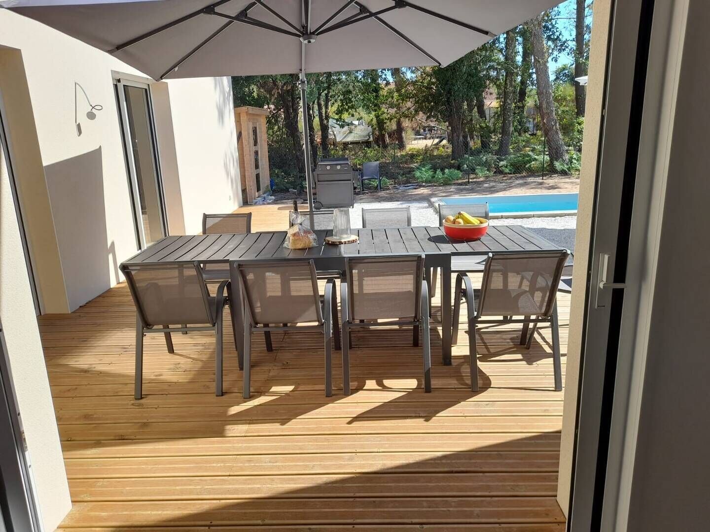 An outdoor patio with a wooden deck, a table with chairs, and a pool in the background.