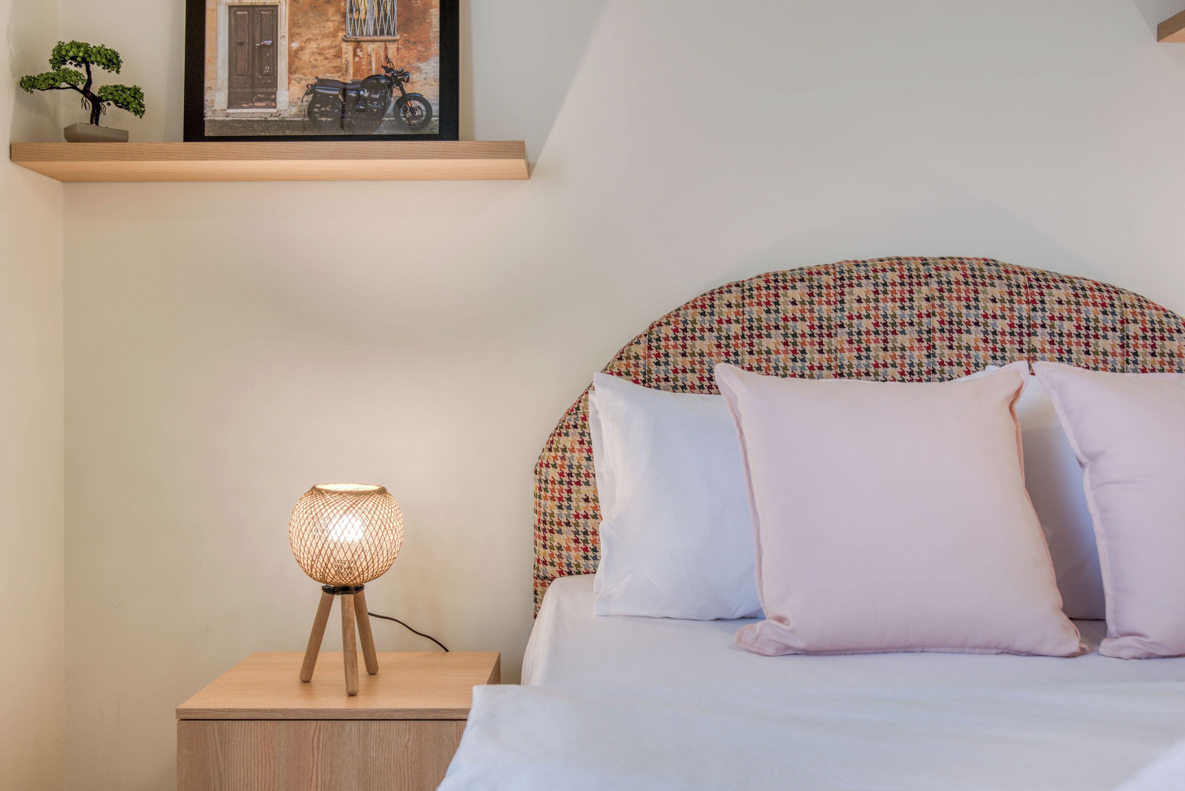 A neatly made bed with a patterned headboard, a bedside lamp, and a framed picture on the nightstand.
