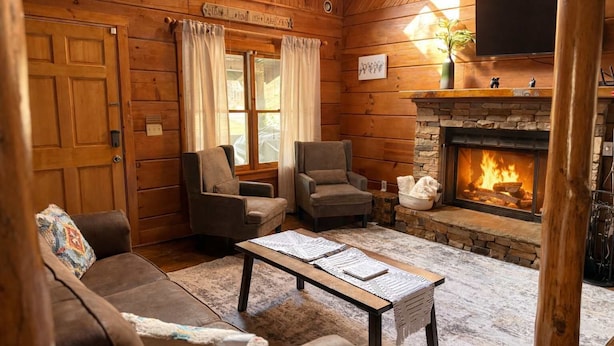 A cozy log cabin interior with a fireplace, two armchairs, a sofa, and a coffee table. - Your Southern Getaway, Sleeps 10・Games, Fire pit (Sevierville)