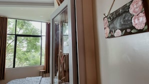 Quarto com uma janela grande, cama com roupa de cama estampada e um letreiro fixado na parede com um design floral.