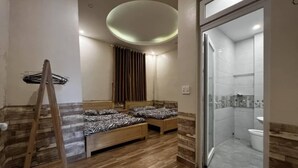 Quarto de hotel com duas camas, chuveiro e escada de madeira.