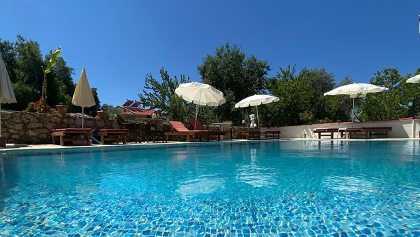 A clear blue pool with tiled flooring, surrounded by lounge chairs and umbrellas.