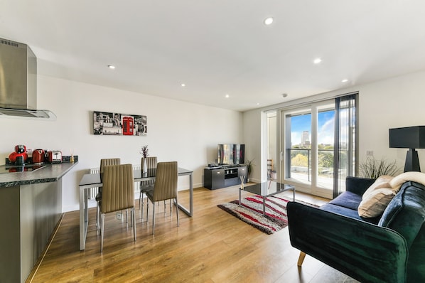 A modern living room with a dining area, a kitchen, and a large window offering a city view.