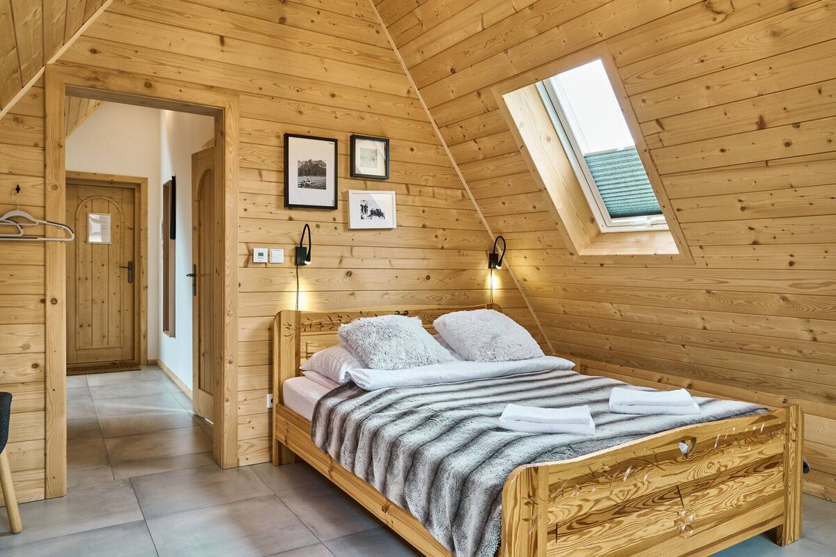 A wooden-paneled bedroom with a bed, a skylight, and framed pictures on the wall.