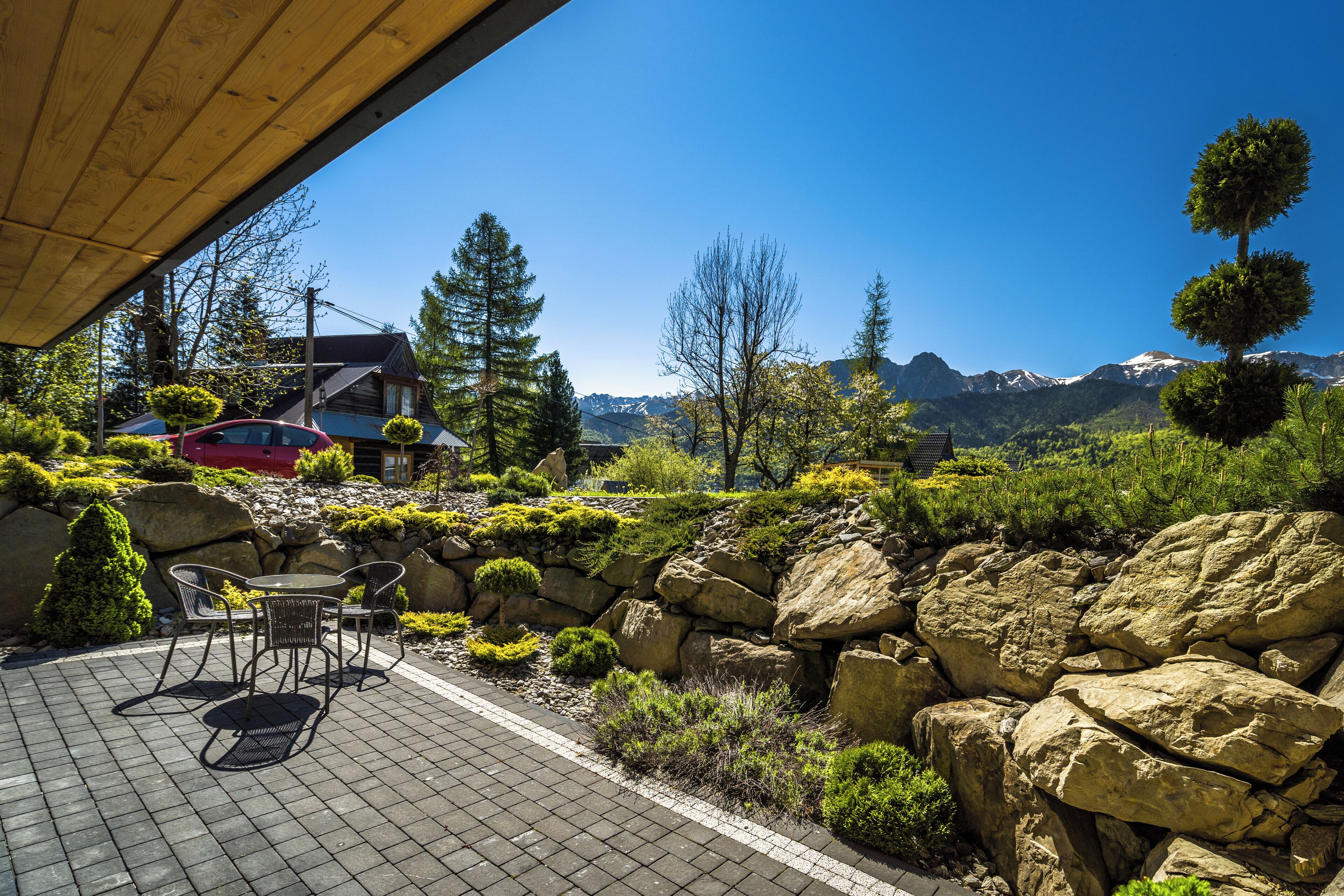 A patio with a table and chairs, surrounded by rocks and greenery, overlooking a mountainous landscape.