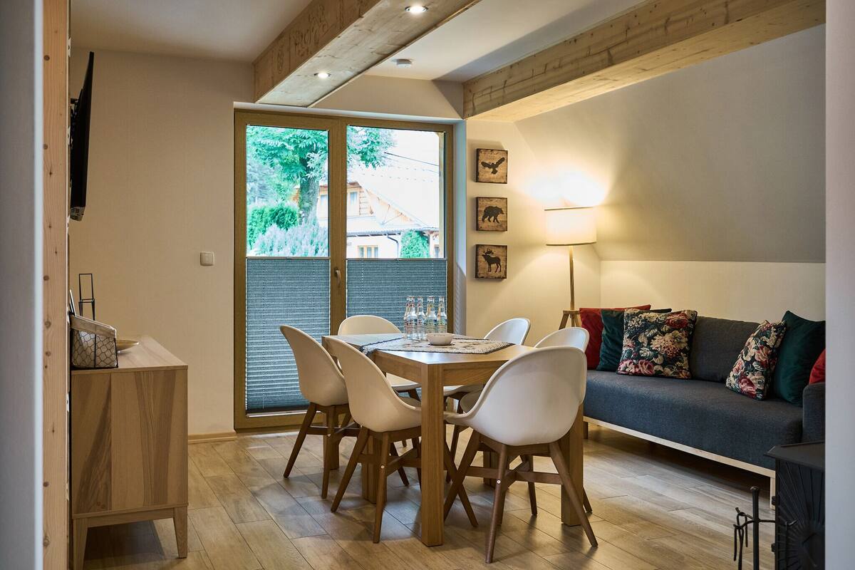 A dining area with a wooden table and chairs, a sofa, and a TV mounted on the wall.
