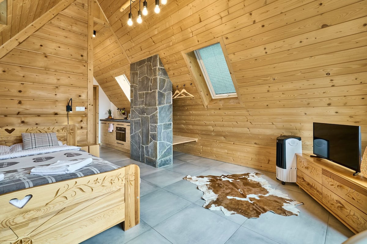 A wooden cabin bedroom with a bed, a stone pillar, a TV, and a heater.