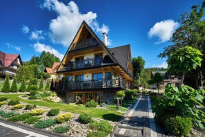 A two-story house with a balcony, surrounded by well-maintained gardens and a clear sky. - Willa Wojdyłówka (Koscielisko)