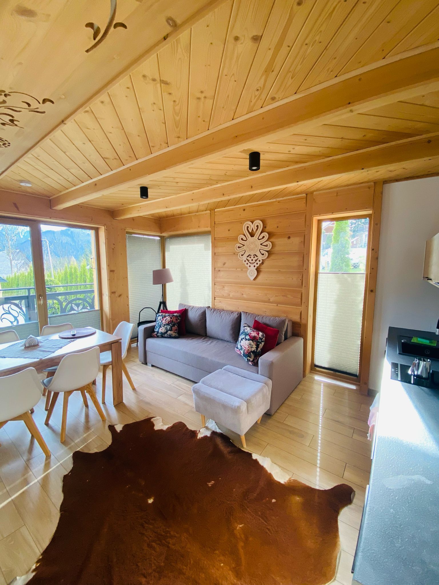 A cozy cabin interior with a wooden ceiling, a sofa set, a dining table, and a large cowhide rug.