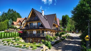 Ein zweistöckiges Haus mit Balkon, umgeben von einem angelegten Garten und einem Parkplatz.