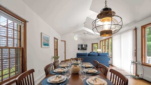 A dining area with a wooden table set for six, a ceiling fan, and a large window with blinds.