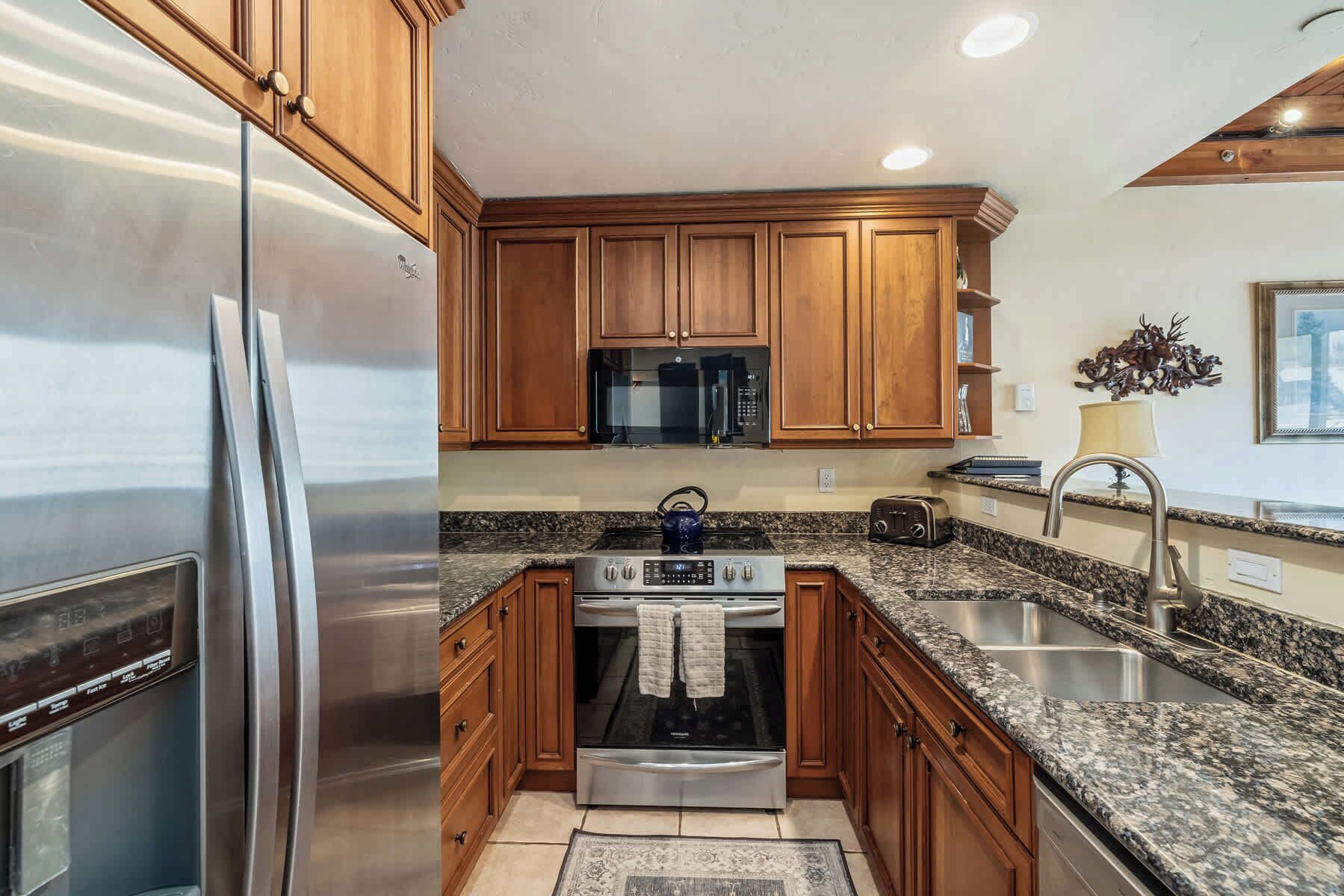 A modern kitchen with wooden cabinets, stainless steel appliances, granite countertops, and a built-in microwave.