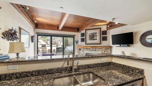A kitchen with granite countertops, a stainless steel sink, wooden ceiling beams, and a view of the outside.