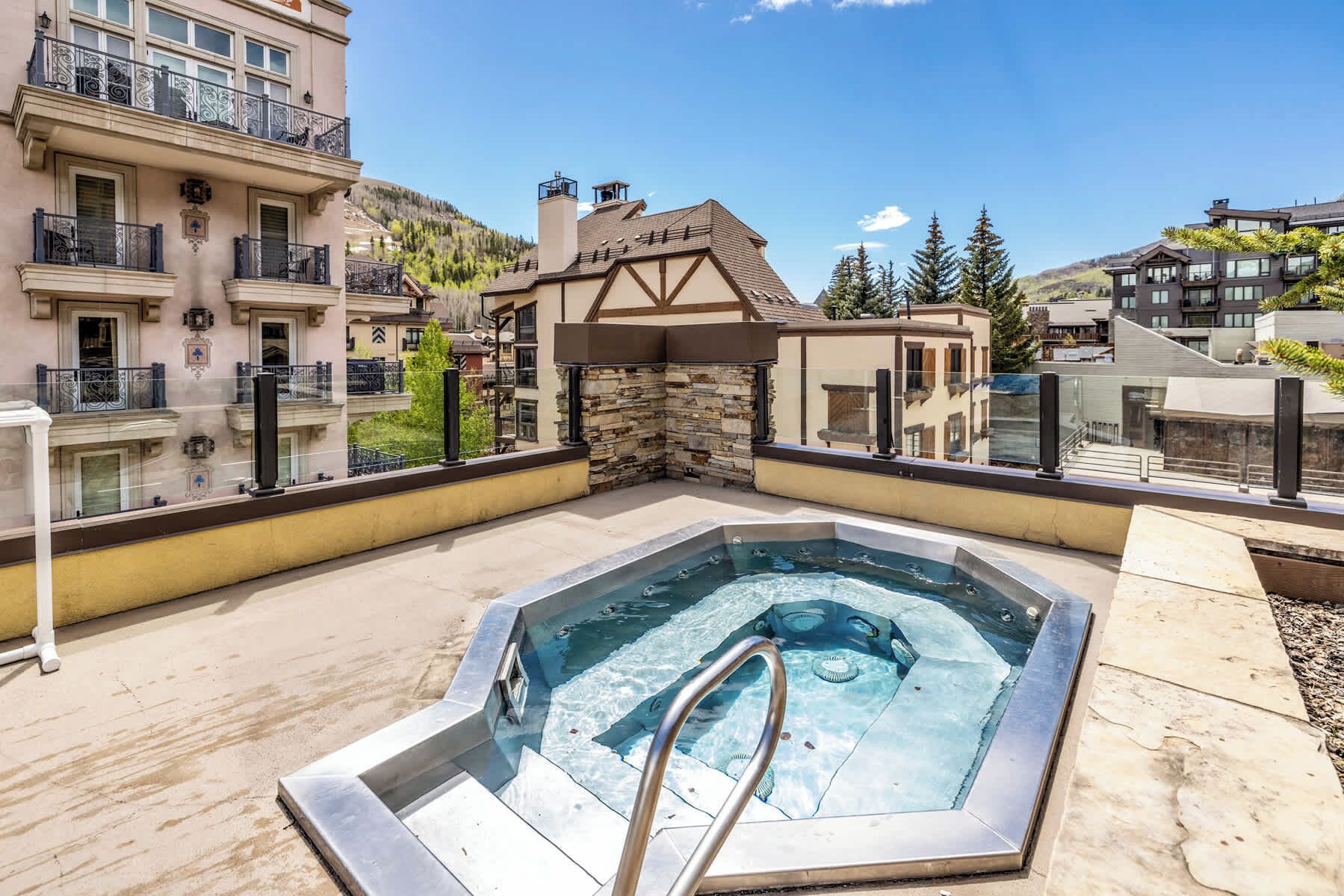 A rooftop pool with a stone wall and a metal ladder, surrounded by buildings and trees.