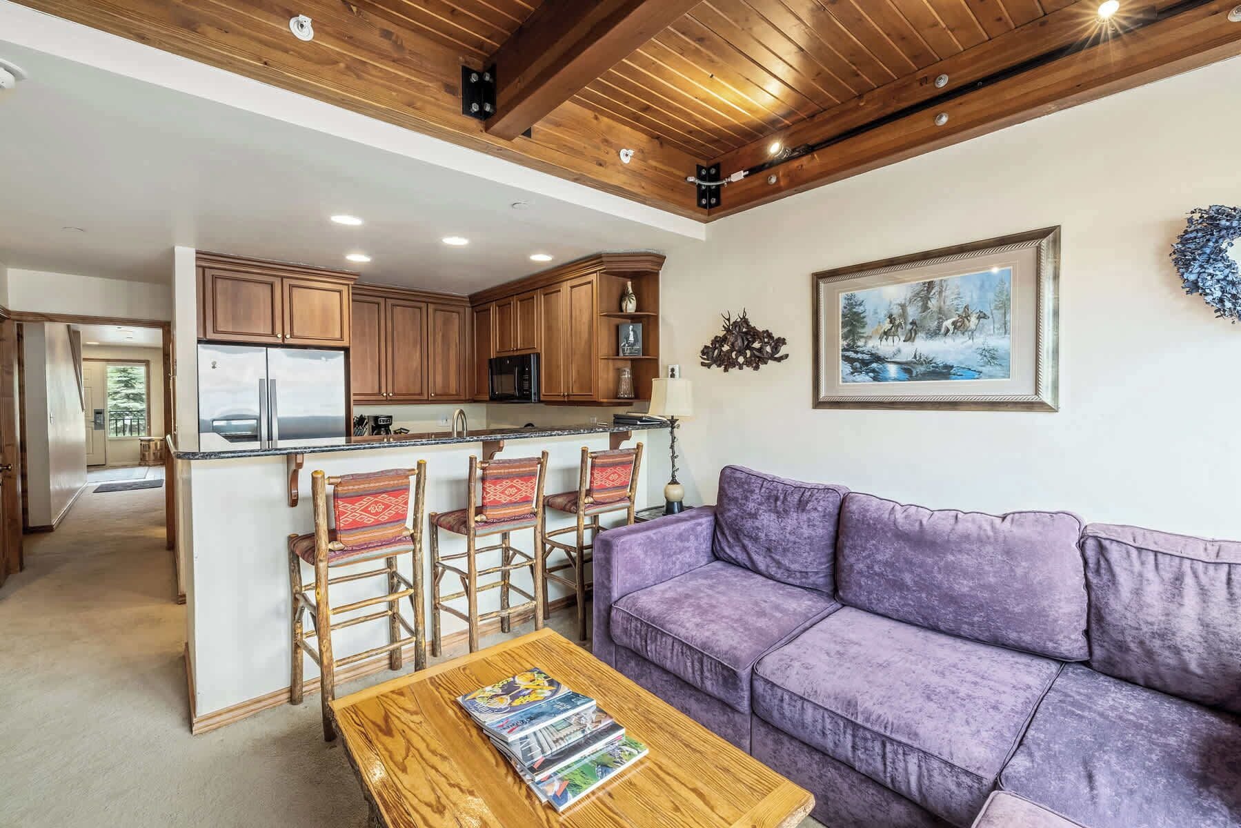 Eine moderne Küche mit Holzschränken, einer zentralen Kochinsel und einem Essbereich mit einem violetten Sofa und Holzsesseln.