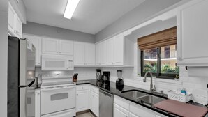 A modern kitchen with white cabinets, stainless steel appliances, and a black countertop. - 2B/2B ISLAND VACATION CONDO-RESORT POOL! WALK TO BEACH! SANTA MARIA 203 (Fort Myers Beach)
